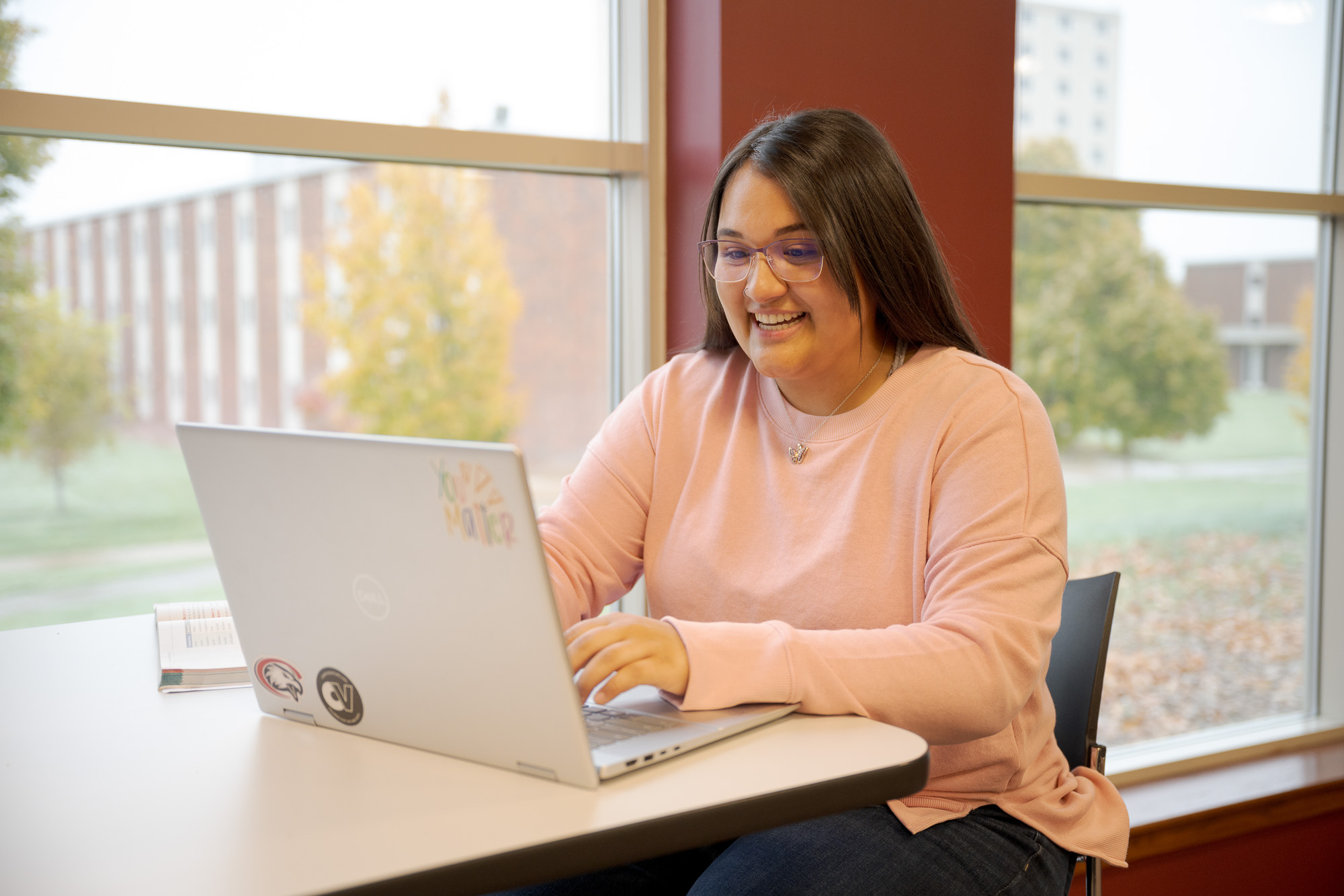 A student sitting at a table, typing on her laptop.